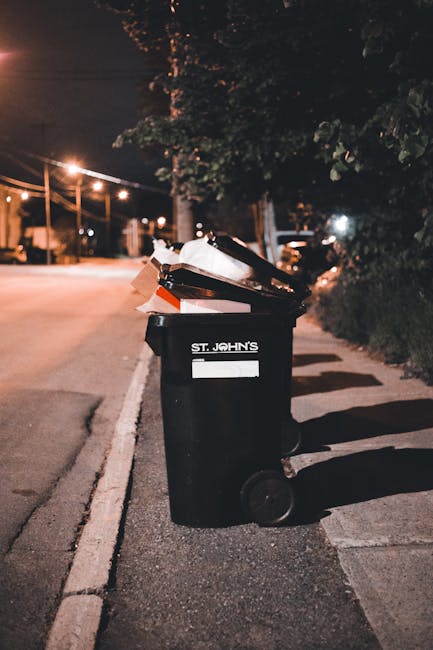 A patch of ground adjacent to a sloped grassy area is littered with discarded cardboard boxes, many crushed or torn, predominantly green with white star logos, and scattered paper debris. Some of the 